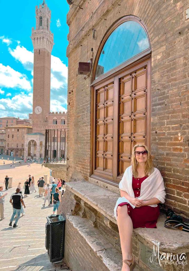 Marina wearing red dress and scarf with main square view of Siena near Florence, Italy behind her