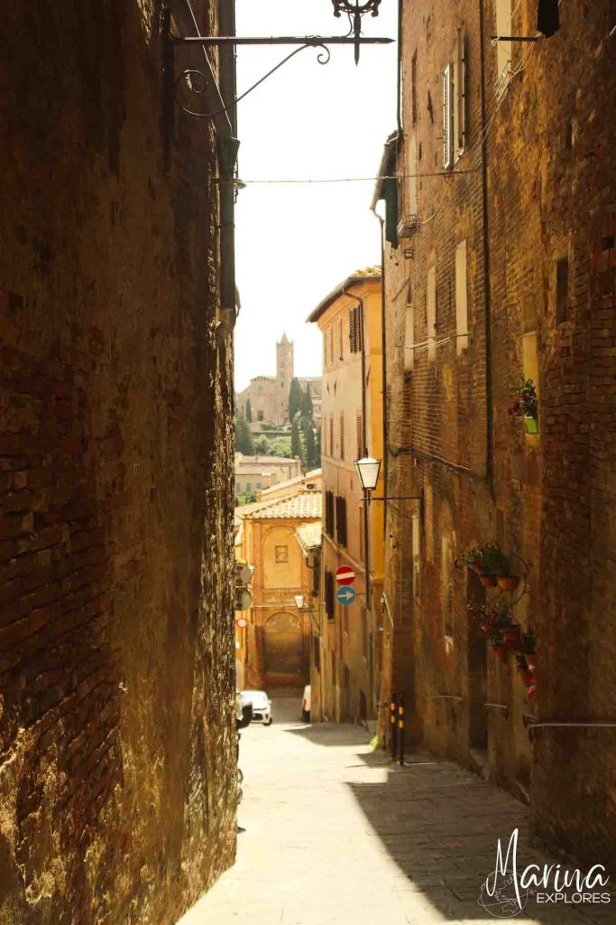 Looking down narrow street in Siena with bell tower in distance near Florence, Italy